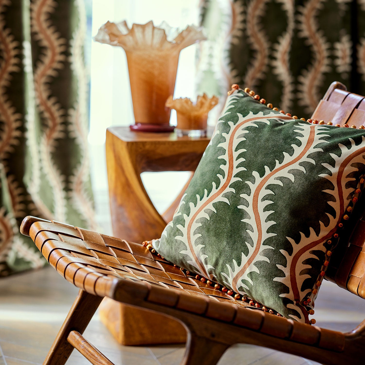 Cushion in a printed velvet fabric in green and orange featuring a stylized fern pattern.