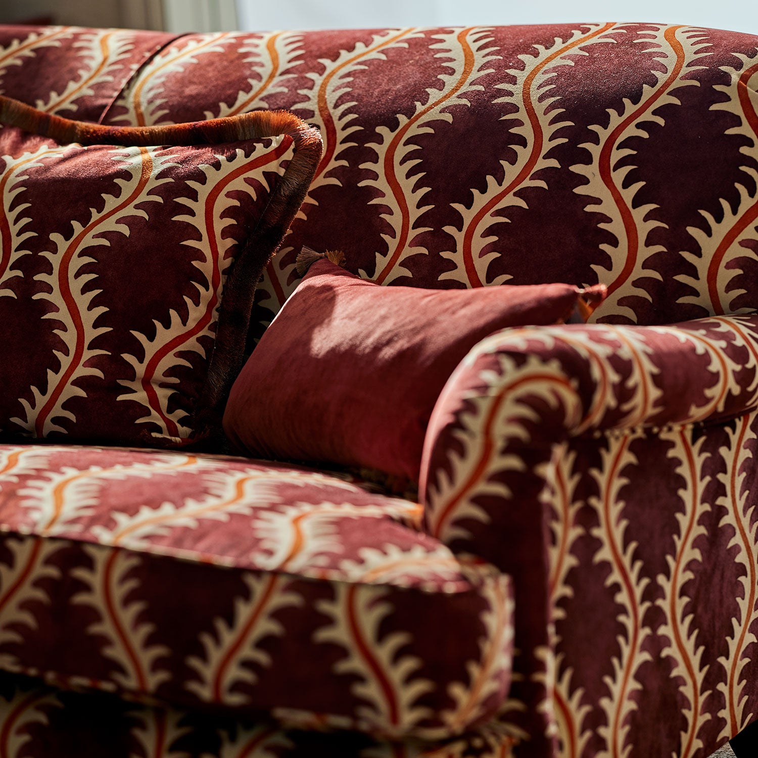 Sofa upholstered in a printed velvet fabric in purple and orange featuring a stylized fern pattern.