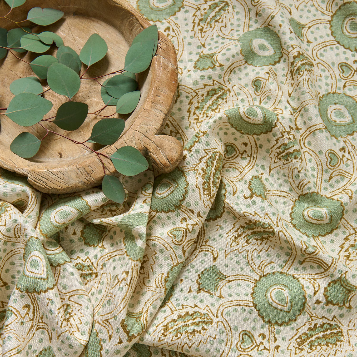 A stylised floral printed on linen fabric in green, orange and cream