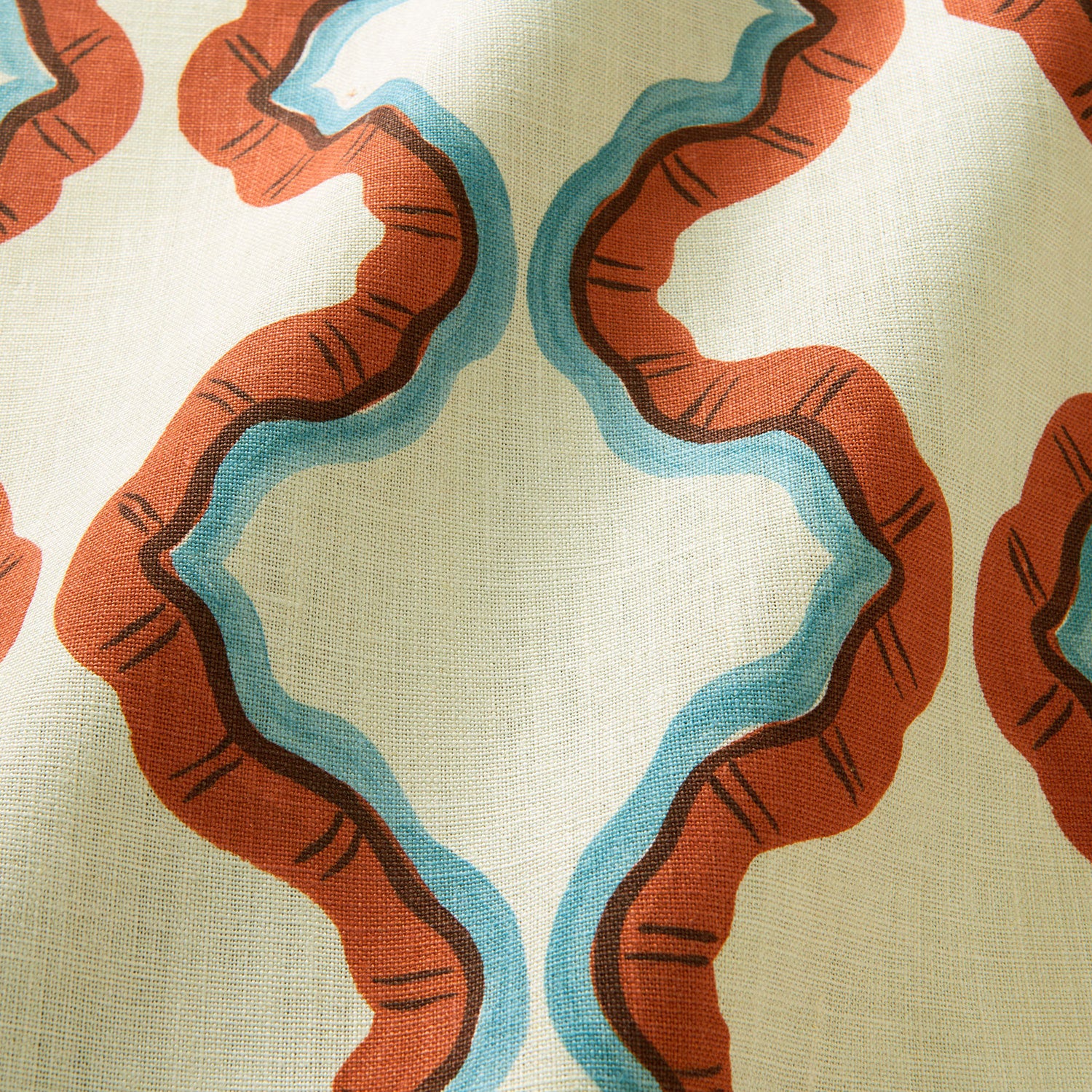 A printed linen fabric sample in blue, orange, brown and off white featuring a mirrored ribbon pattern.
