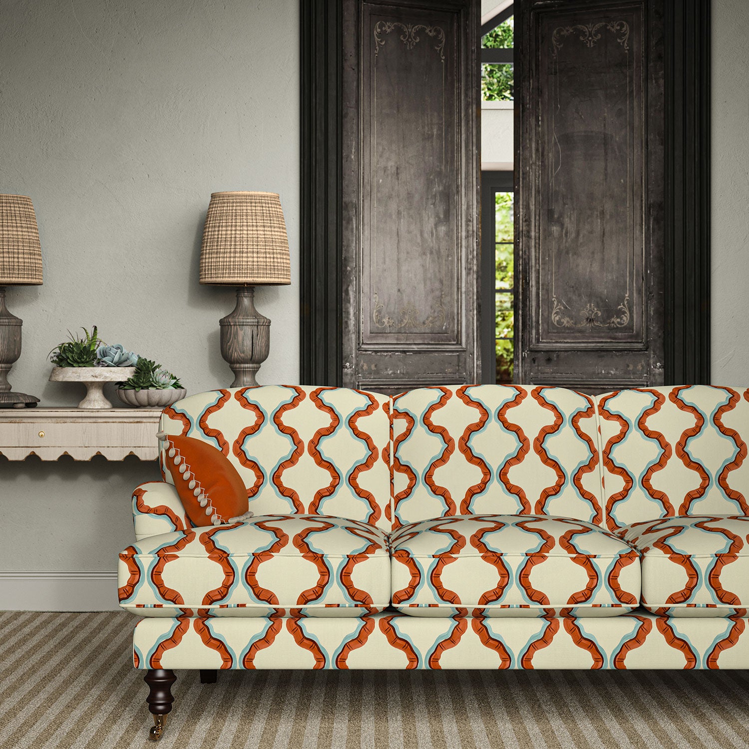 Sofa upholstered in a printed linen fabric in blue, orange, brown and off white featuring a mirrored ribbon pattern.
