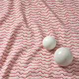 A printed linen fabric sample in pink, red and off white featuring a sound wave pattern