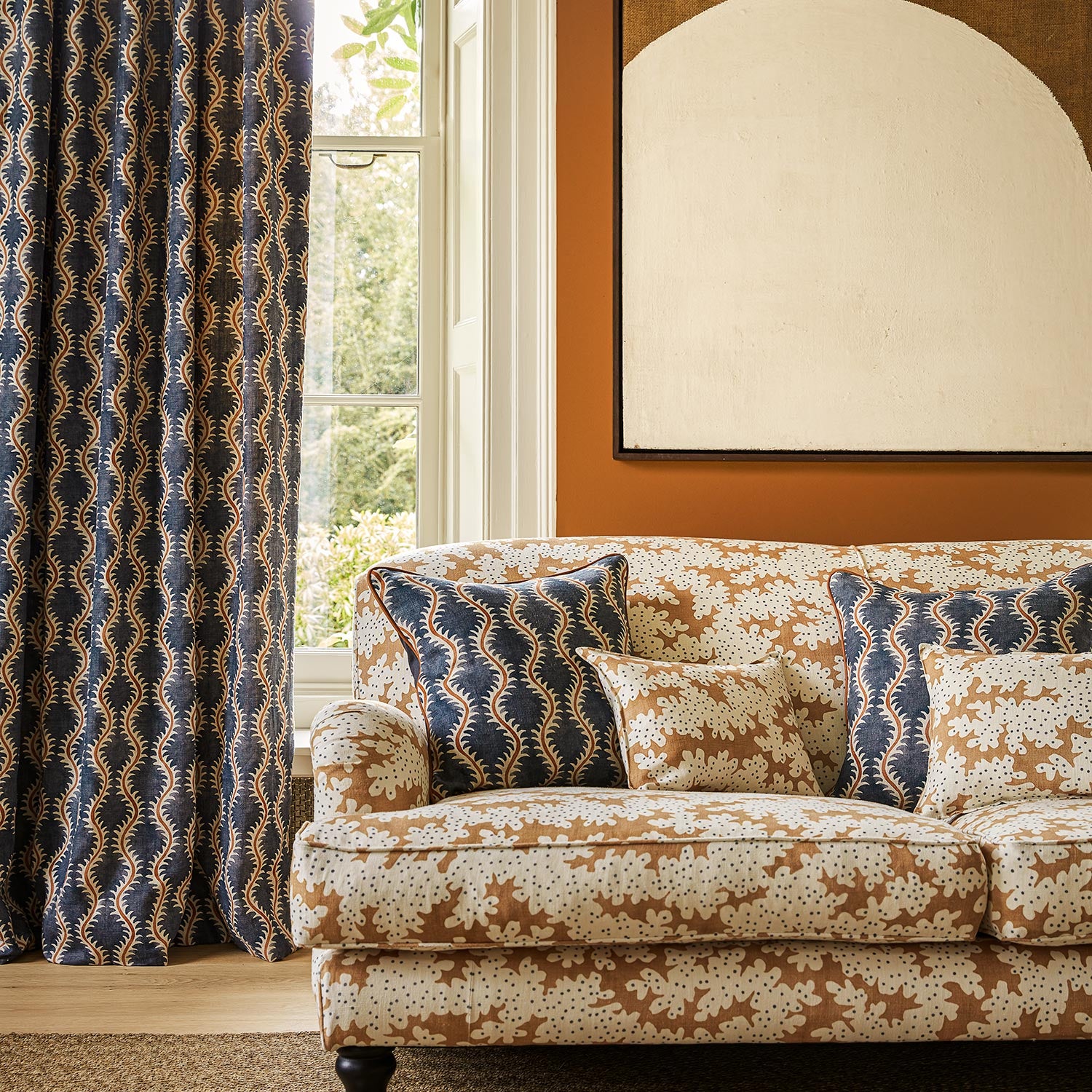 Sofa upholstered in a printed linen fabric sample in orange, blue and off white featuring a stylized coral pattern.