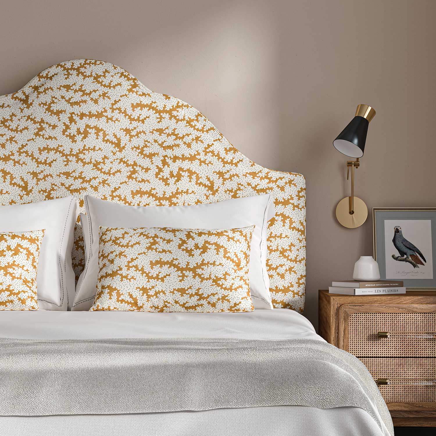 Headboard upholstered in a printed linen fabric sample in orange, blue and off white featuring a stylized coral pattern.