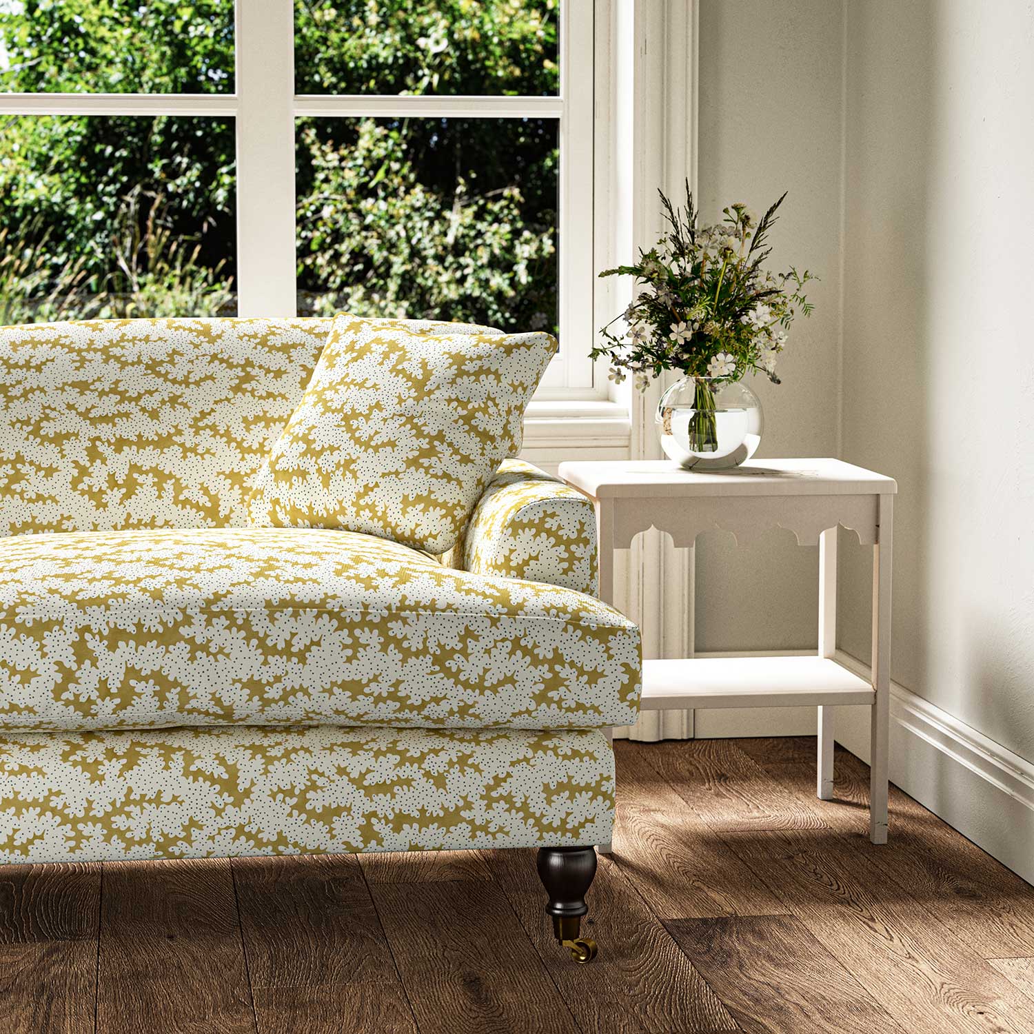 Sofa upholstered in a printed linen fabric sample in yellow, blue and off white featuring a stylized coral pattern.
