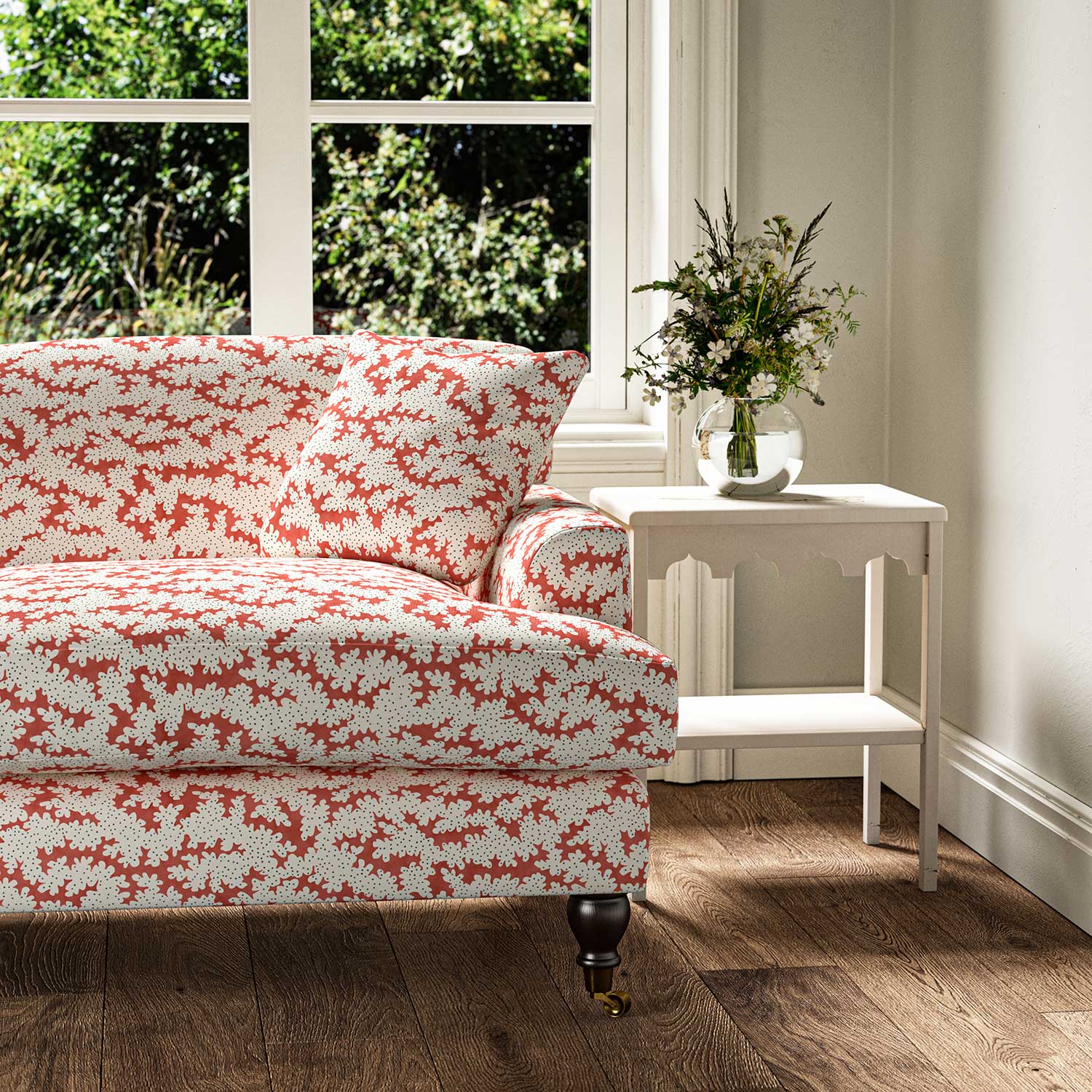 Sofa upholstered in a printed linen fabric sample in red, brown and off white featuring a stylized coral pattern.