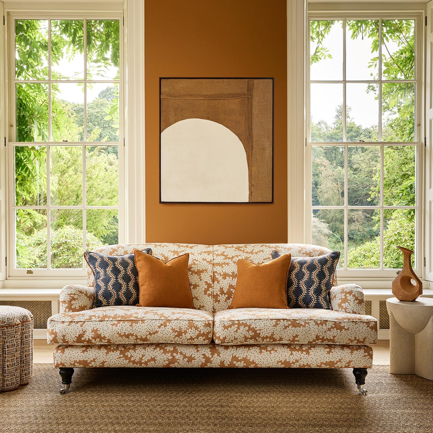 Sofa upholstered in a printed linen fabric sample in orange, blue and off white featuring a stylized coral pattern.