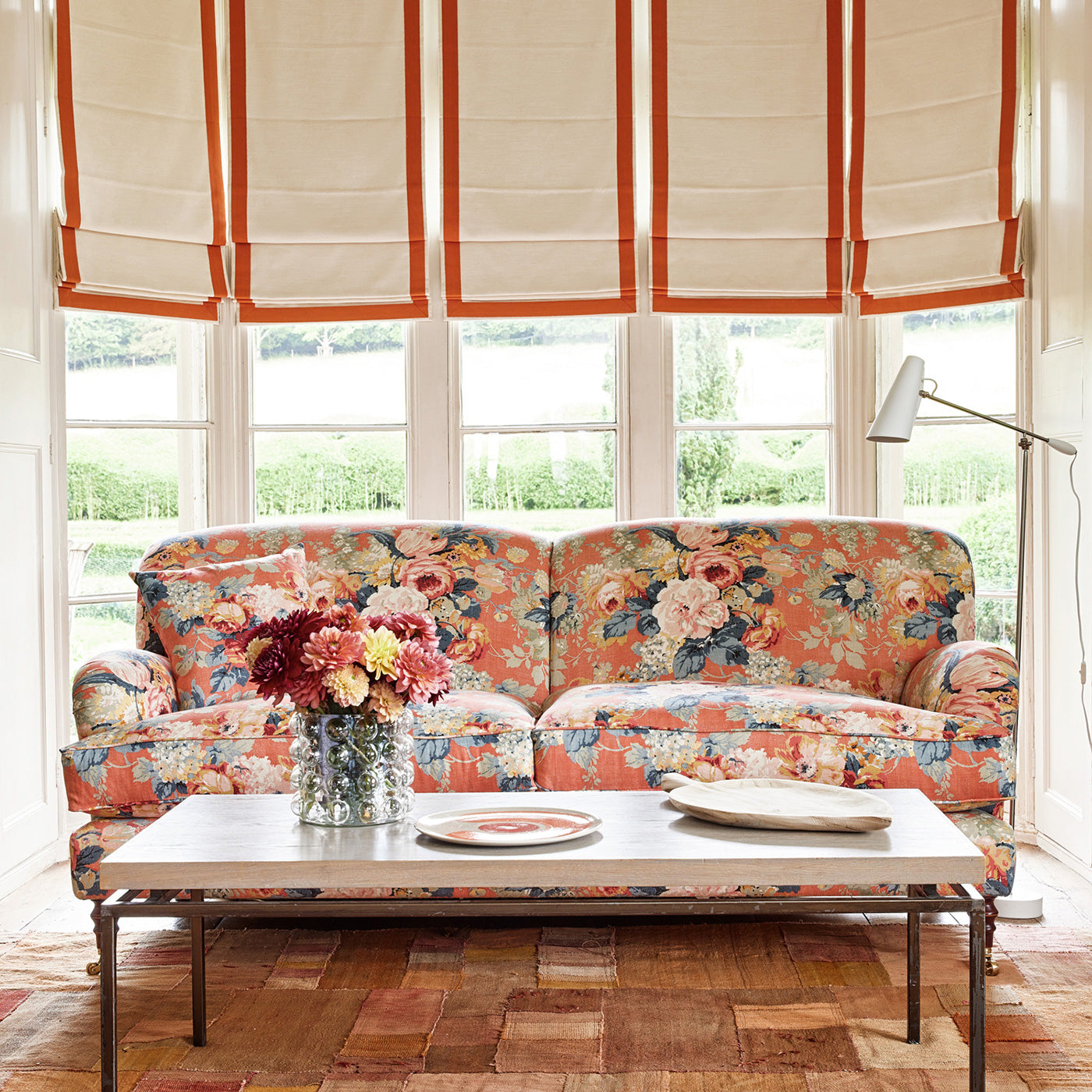 Sofa covered in a printed linen fabric with bouquets of roses on an orange backdrop.