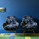 Two chairs covered in a printed velvet fabric showcasing a rich, tropical-style toile in Indigo.