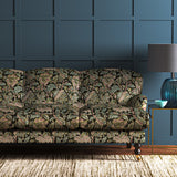 A printed velvet fabric showcasing an archival document, circa 1700s, this stylised floral is lavish, graceful, and timeless in brown, blue, pink and green on a sofa