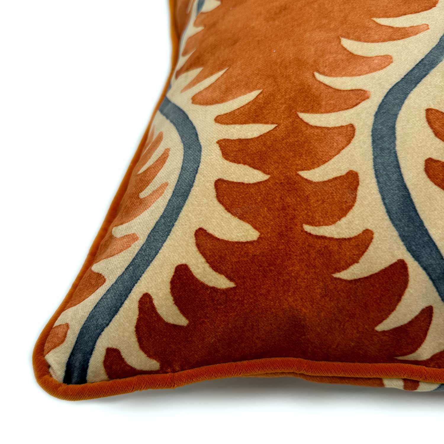 A orange, blue and off white velvet cushion with a all-over repeat pattern and velvet piping.