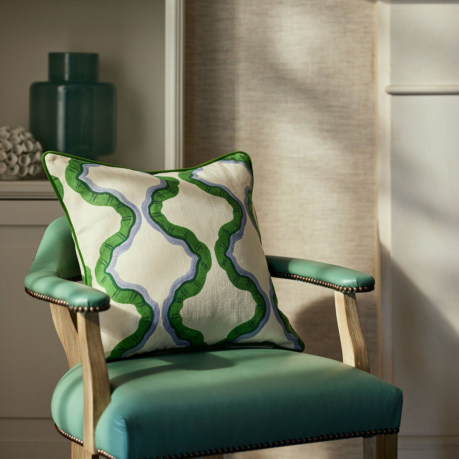 A green, blue and off white linen cushion featuring a mirrored ribbon pattern with a velvet piping.