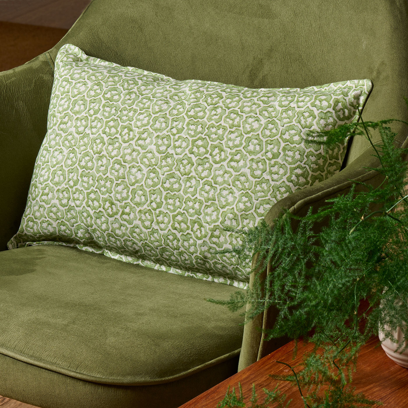 A green and cream linen cushion with a block print pattern.