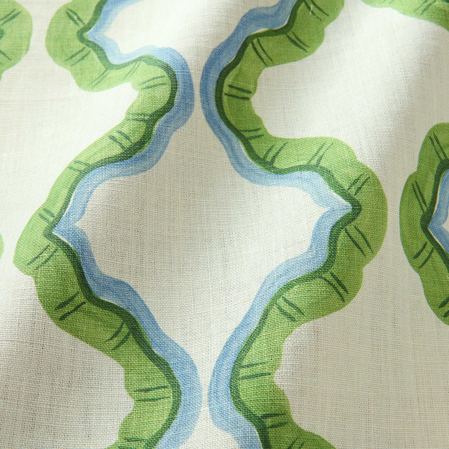 A printed linen fabric sample in blue, green, and off white featuring a mirrored ribbon pattern.