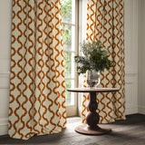 Curtains made from a printed linen fabric in orange, brown, and off white featuring a mirrored ribbon pattern.
