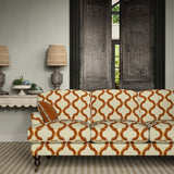 Sofa upholstered in a printed linen fabric in orange, brown, and off white featuring a mirrored ribbon pattern.