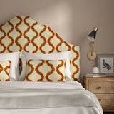 Headboard upholstered in a printed linen fabric in orange, brown, and off white featuring a mirrored ribbon pattern.