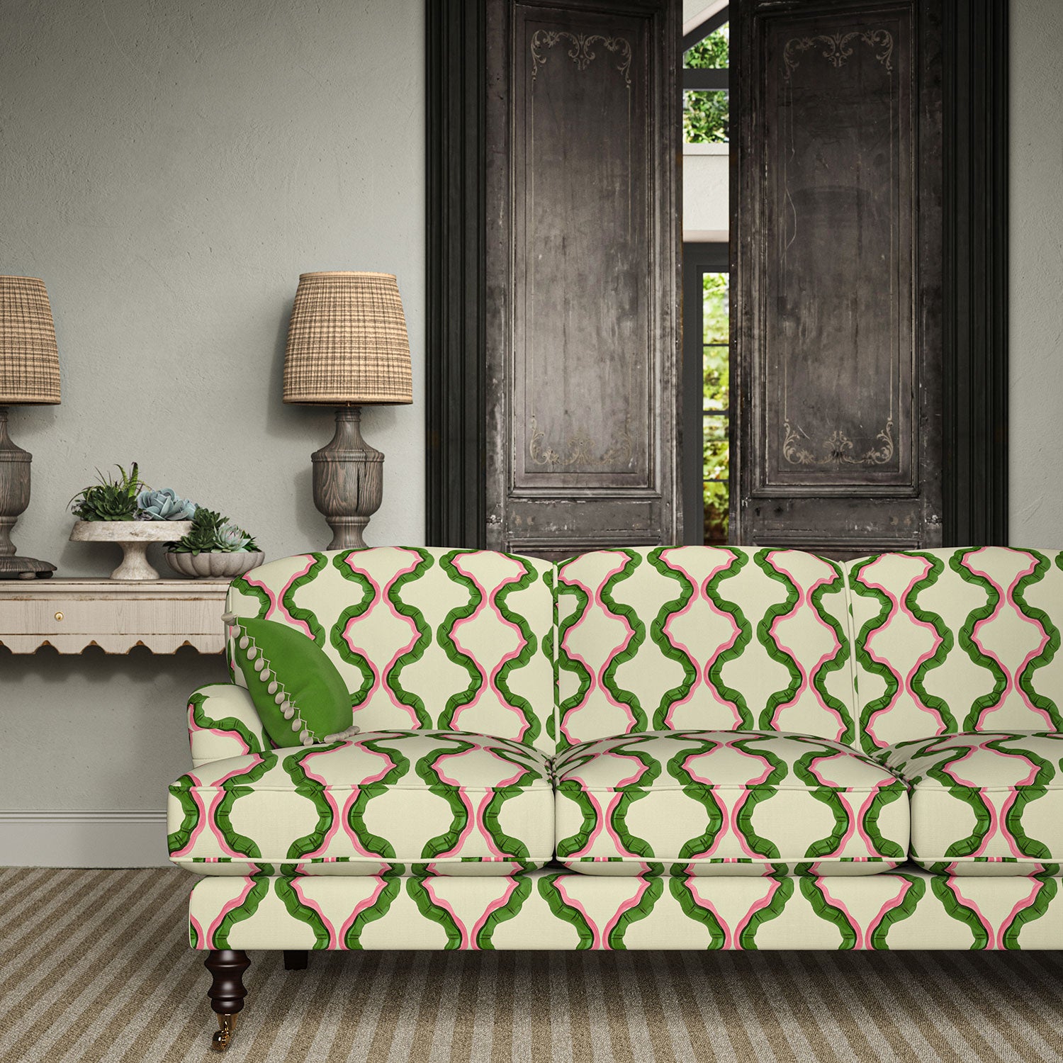 Sofa upholstered in a printed linen fabric in pink, green, and off white featuring a mirrored ribbon pattern.