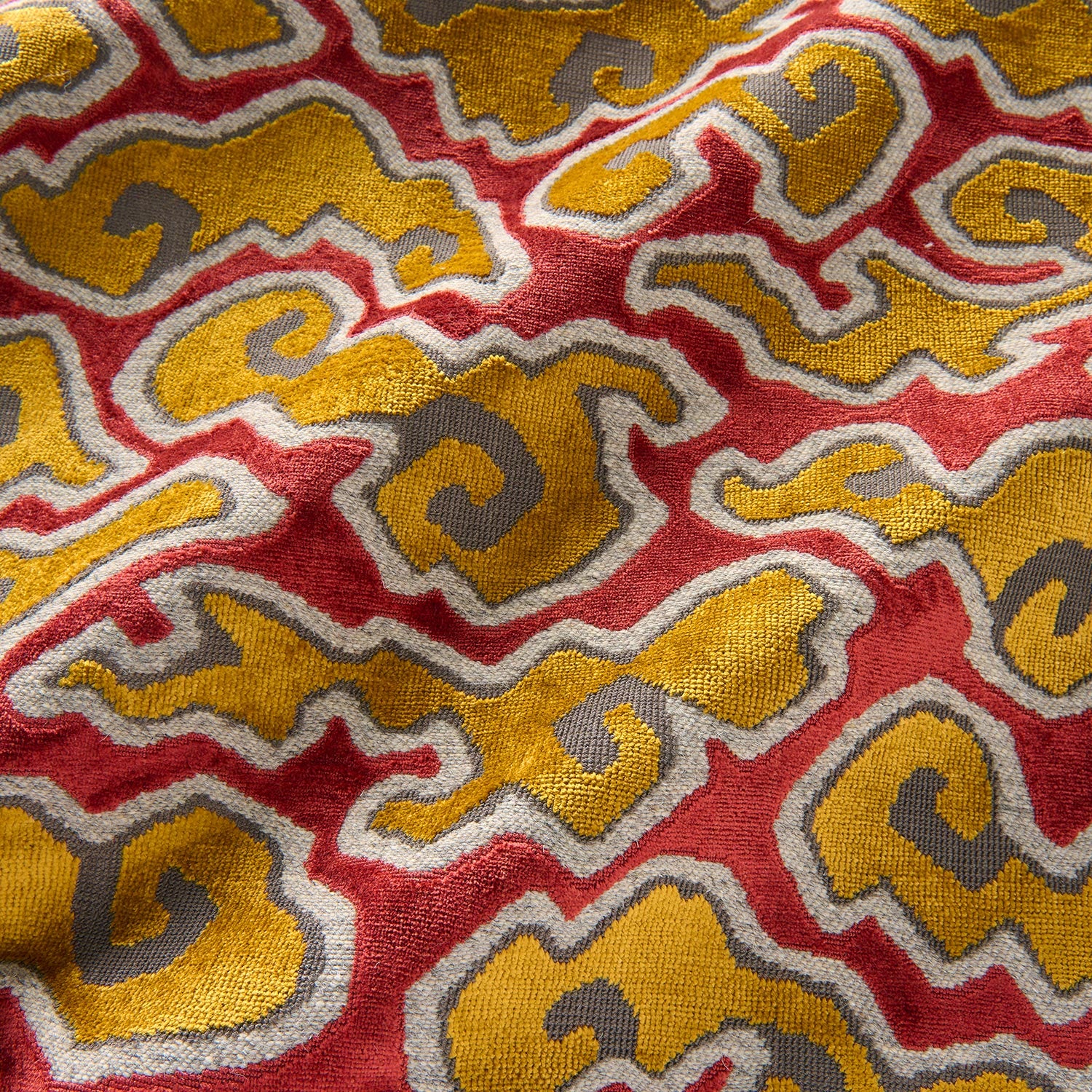 A woven velvet fabric sample in red, yellow and brown featuring a stylised cloud pattern.