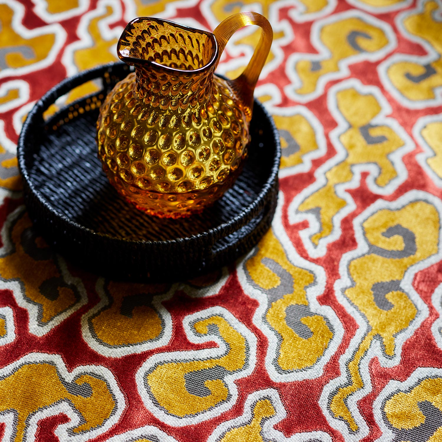 A woven velvet fabric sample in red, yellow and brown featuring a stylised cloud pattern.