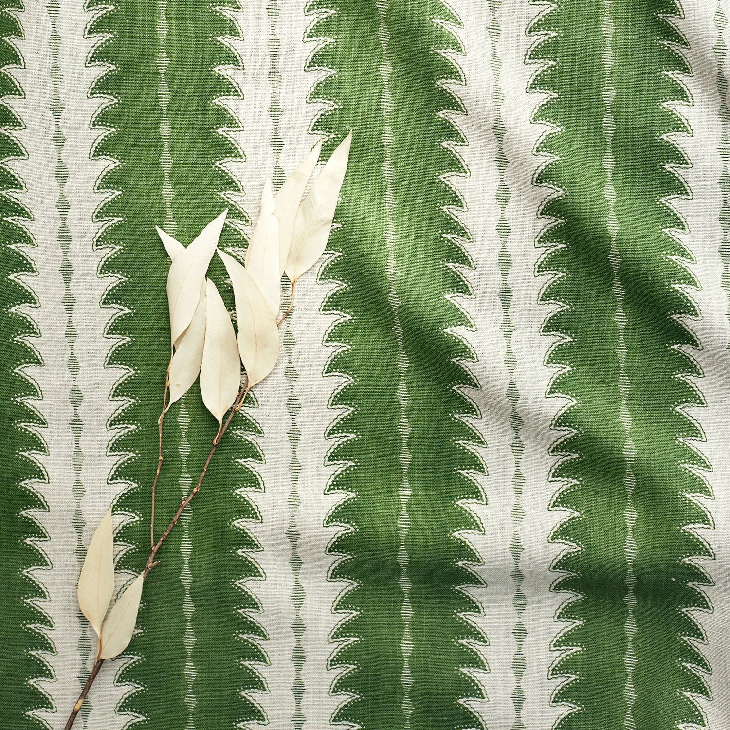 A printed linen fabric sample in green and off white featuring a striped fern design.