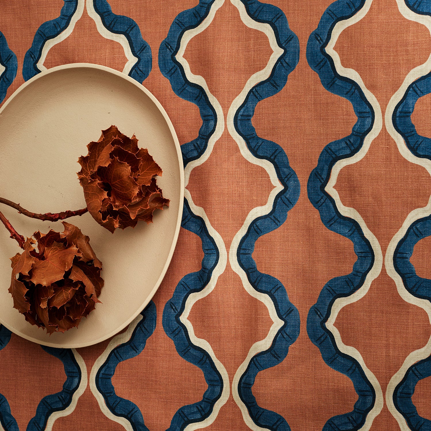 A printed linen fabric sample in blue, orange, black and off white featuring a mirrored ribbon pattern.