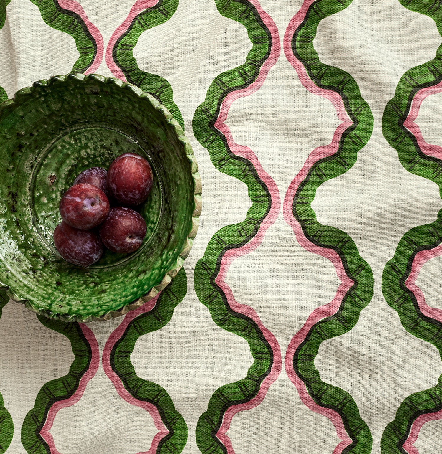 A printed linen fabric sample in pink, green, and off white featuring a mirrored ribbon pattern.