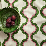 A printed linen fabric sample in pink, green, and off white featuring a mirrored ribbon pattern.
