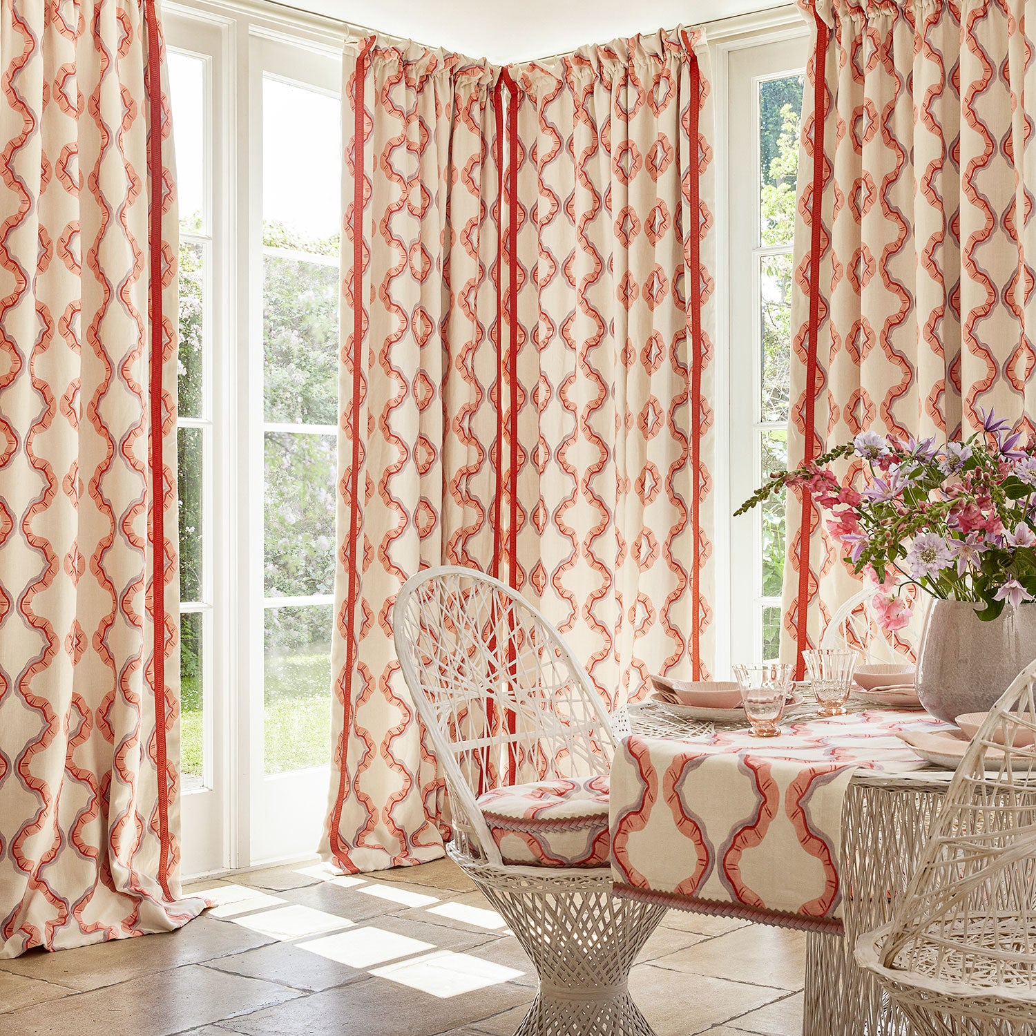 Curtains made from a printed linen fabric in pink, purple, red, and off white featuring a mirrored ribbon pattern.