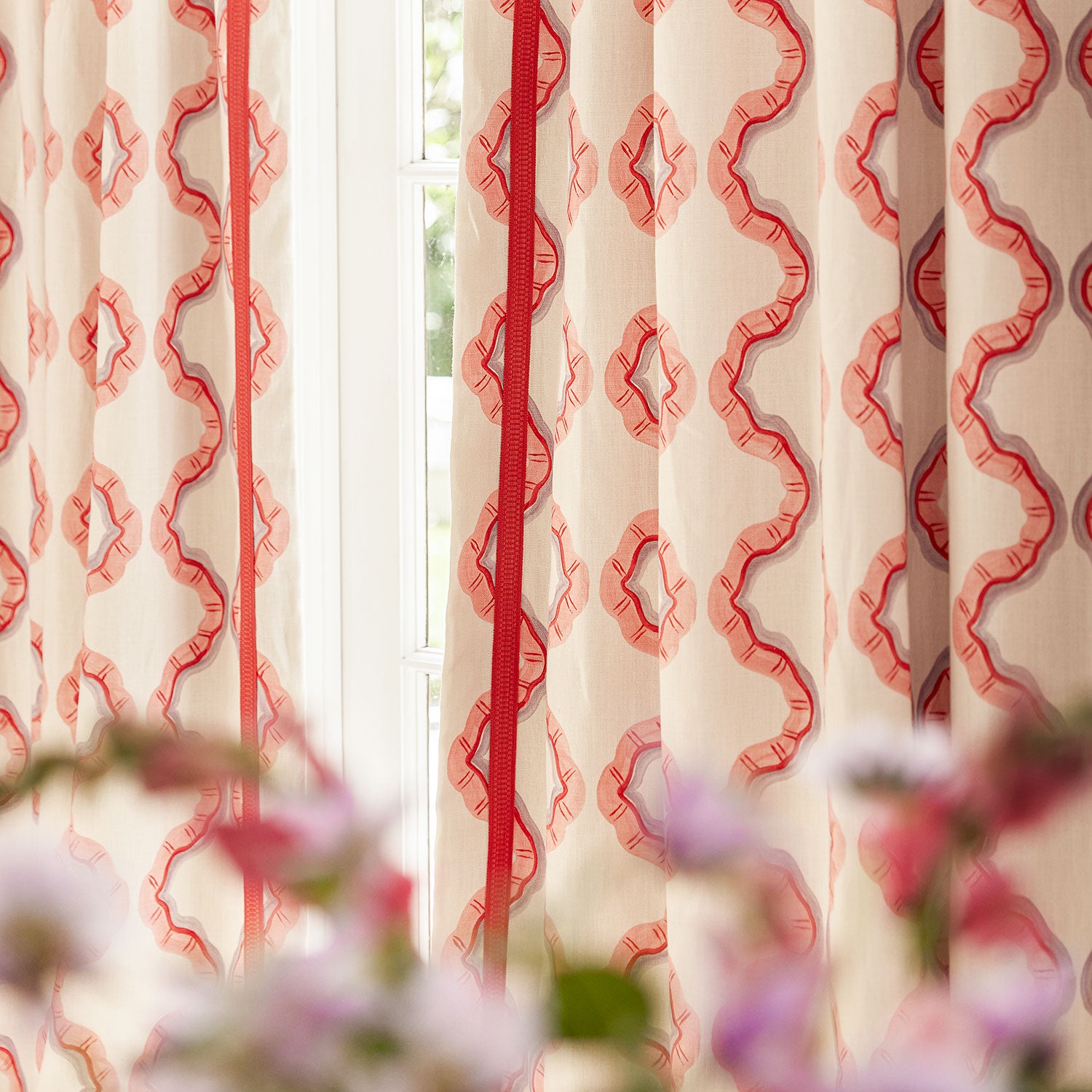 Curtains made from a printed linen fabric in pink, purple, red, and off white featuring a mirrored ribbon pattern.