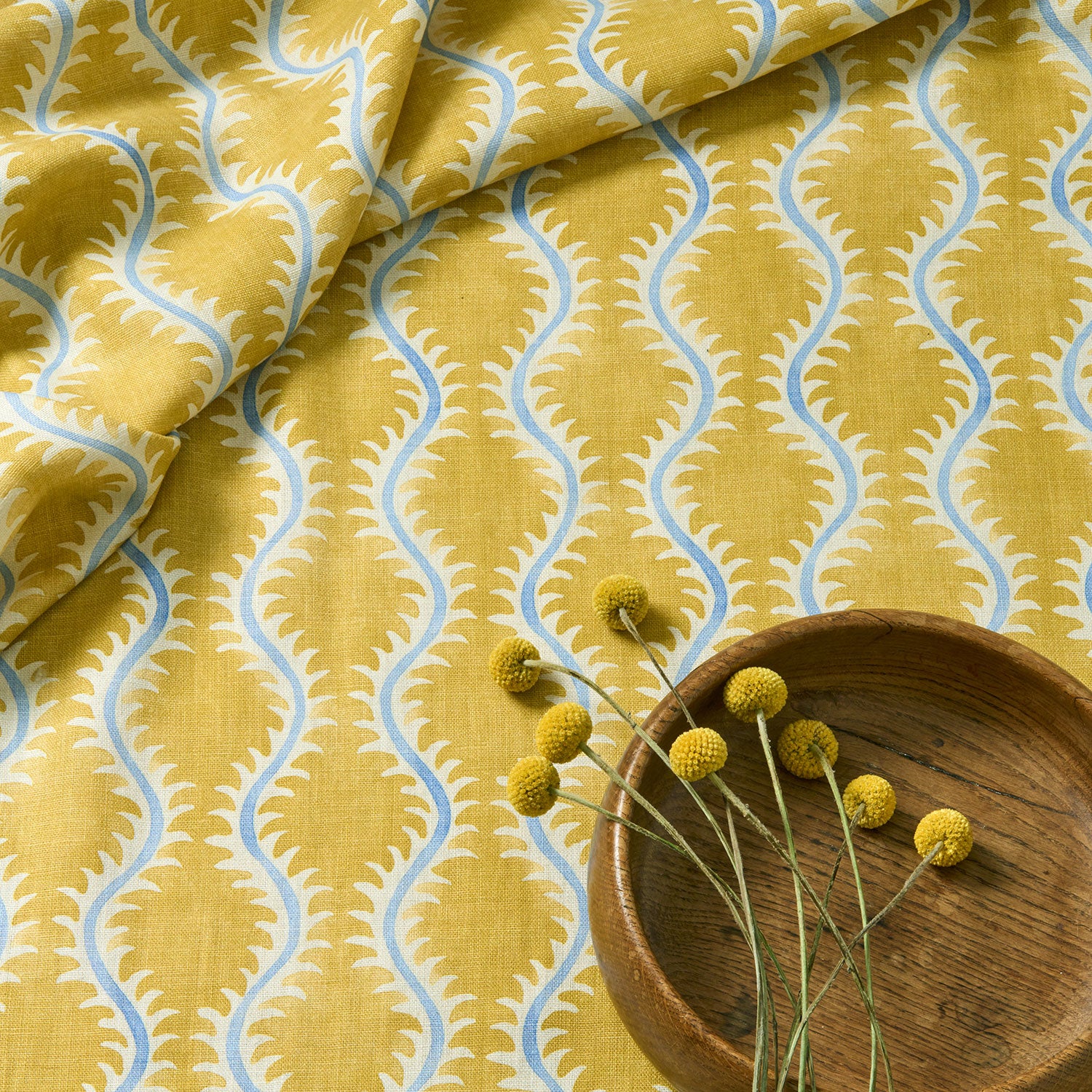 A printed linen fabric sample in yellow, blue and off white featuring a stylized fern pattern.