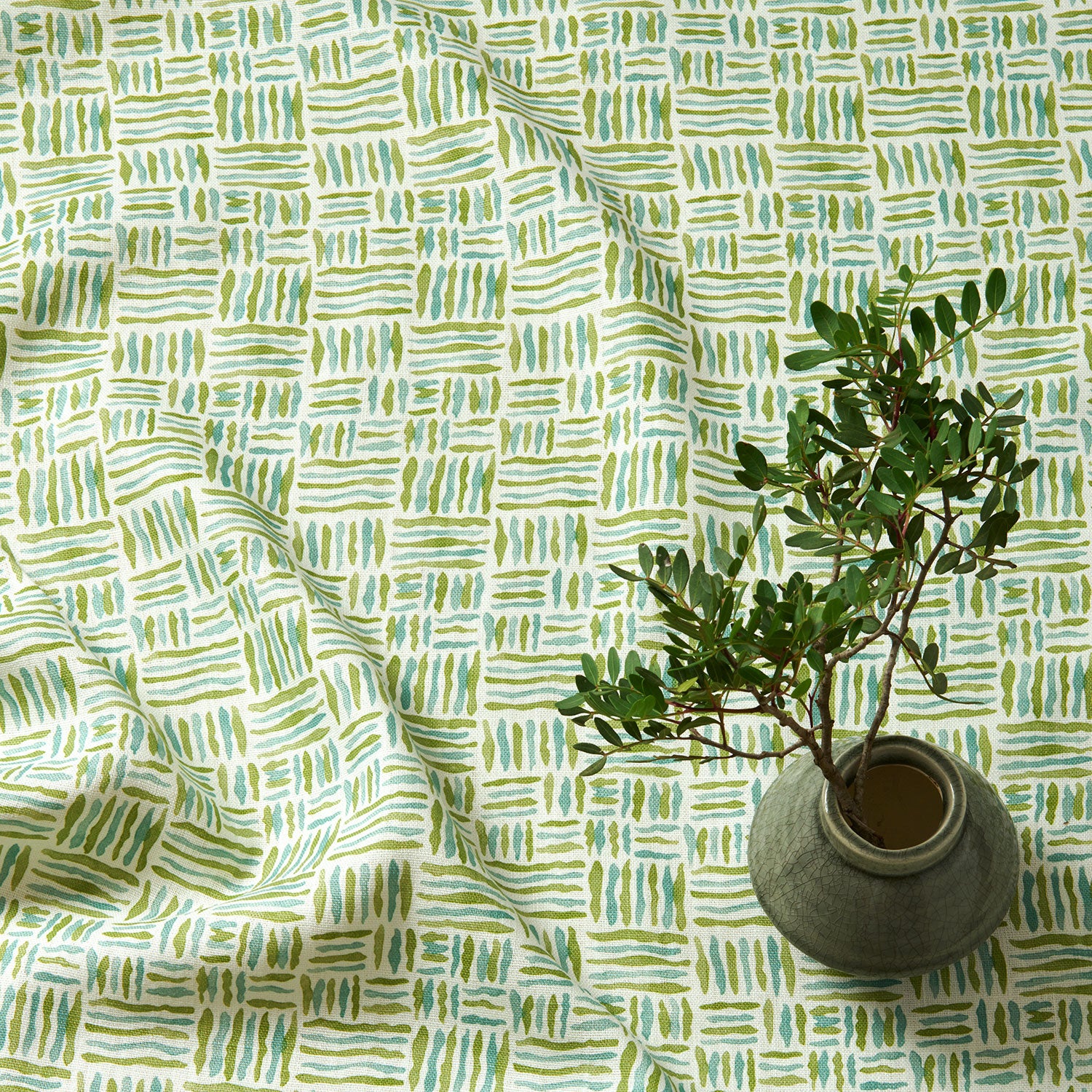 A printed linen fabric sample in green, blue and off white featuring a basketweave pattern.