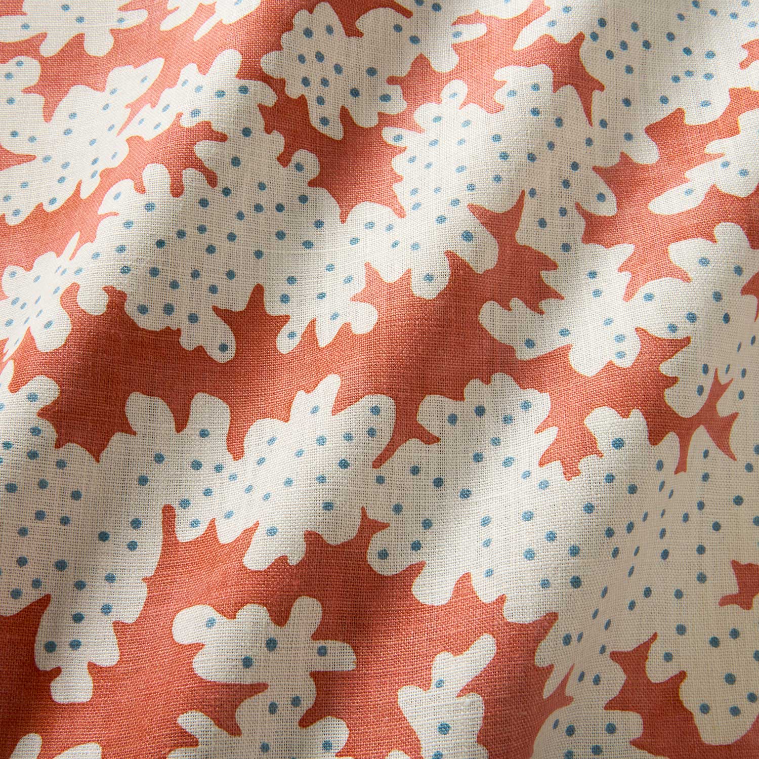 A printed linen fabric sample in orange, blue and off white featuring a stylized coral pattern.