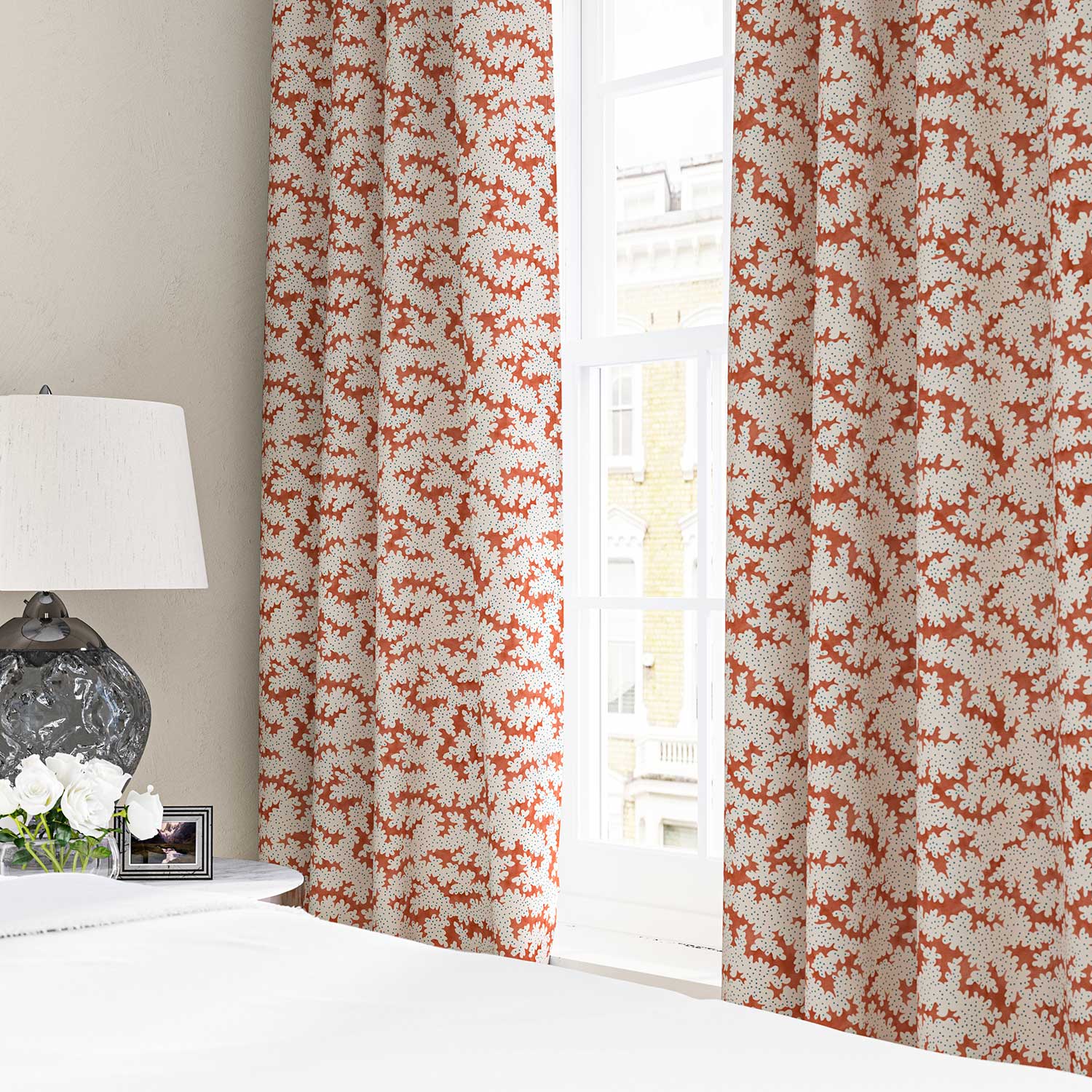 Curtains made from a printed linen fabric sample in orange, blue and off white featuring a stylized coral pattern.