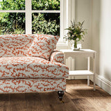 Sofa upholstered in a printed linen fabric sample in orange, blue and off white featuring a stylized coral pattern.