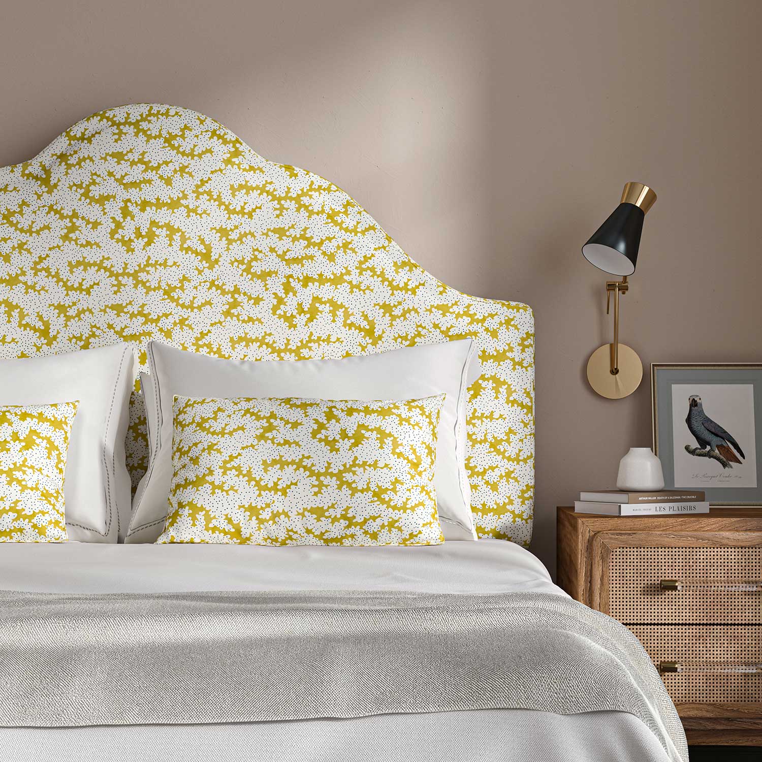 Headboard upholstered in a printed linen fabric sample in yellow, blue and off white featuring a stylized coral pattern.