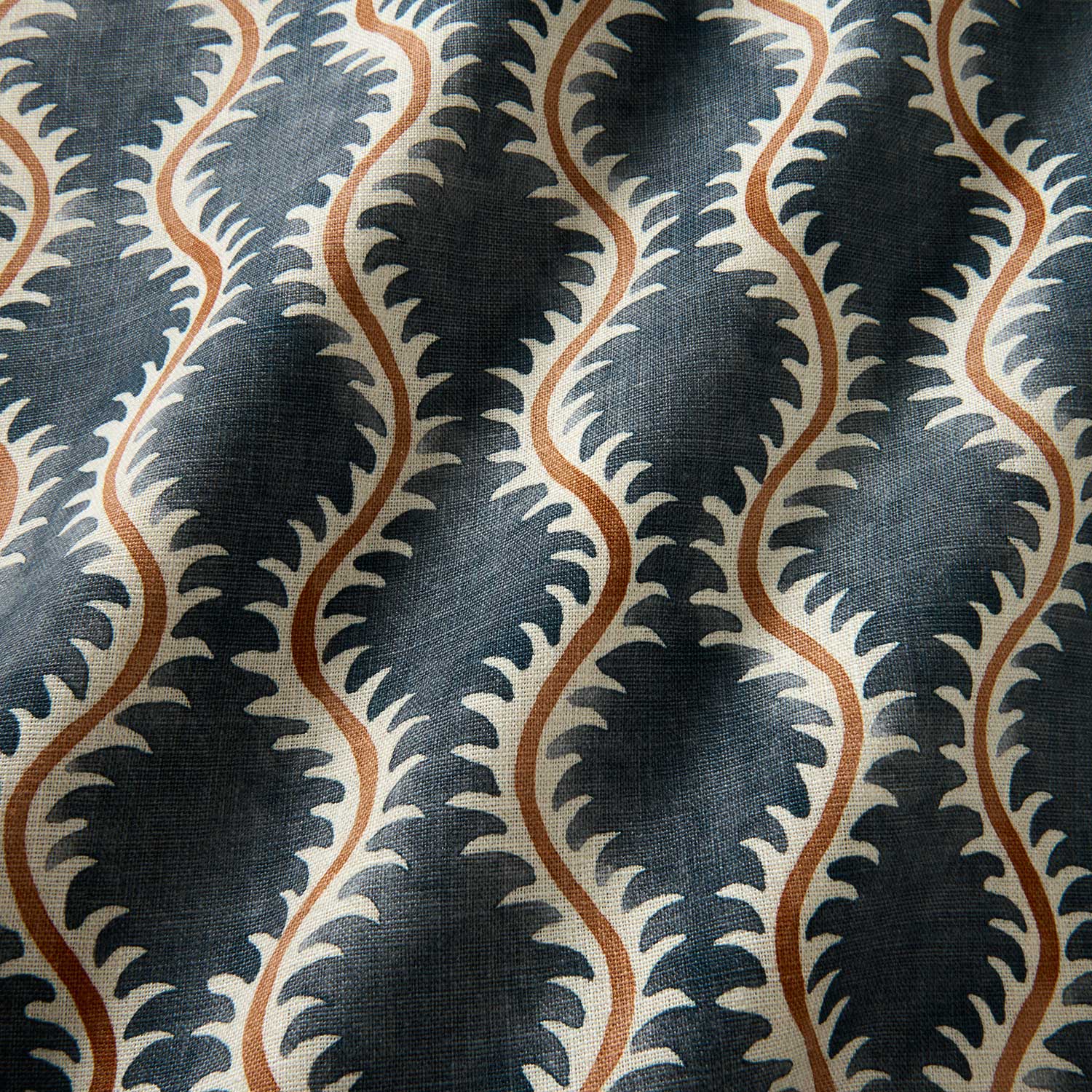 A printed linen fabric sample in blue, orange and off white featuring a stylized fern pattern.