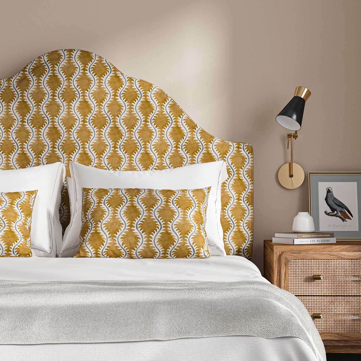 Headboard upholstered in a printed linen fabric sample in orange, blue and off white featuring a stylized fern pattern.
