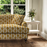 Sofa upholstered in a printed linen fabric sample in orange, blue and off white featuring a stylized fern pattern.