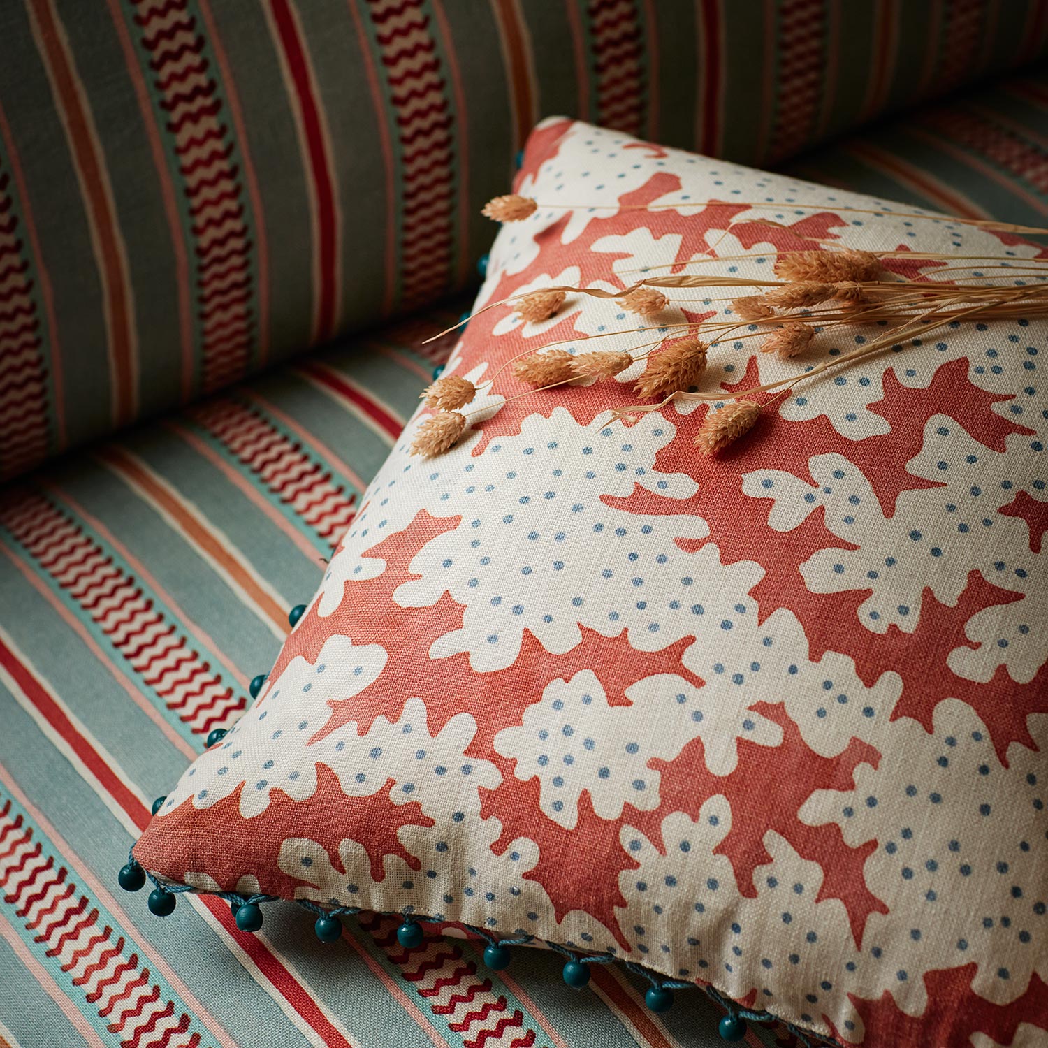 Cushion made from a printed linen fabric sample in orange, blue and off white featuring a stylized coral pattern.