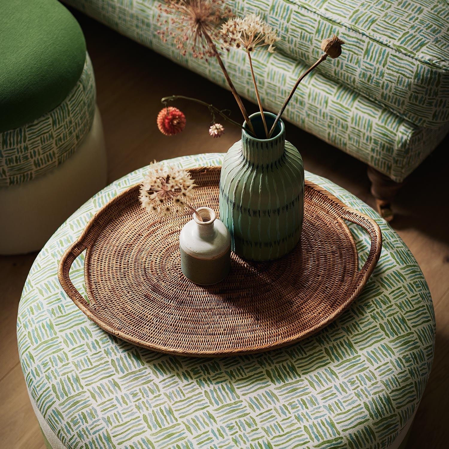 Footstool upholstered in a printed linen fabric in green, blue and off white featuring a basketweave pattern.