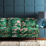 Sofa upholstered in an emerald coloured velvet upholstery fabric with a floral and bird design with a stain resistant finish.
