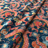Printed velvet fabric with intricate mirror dragon design in orange and blue colours, for upholstery and curtain use.