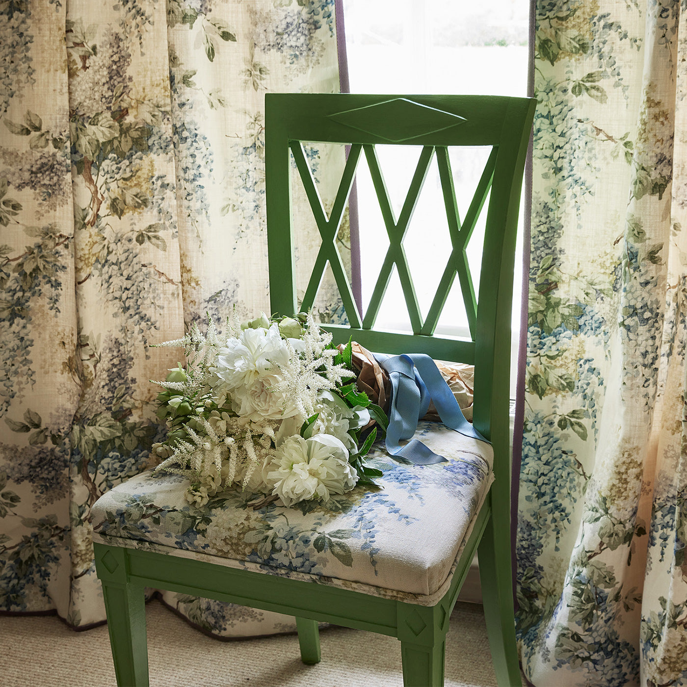 Curtains and chair in a printed linen fabric with a wisteria floral pattern in yellow, green and blue colours.