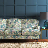 A printed velvet fabric showcasing a beautiful landscape of mountains, willows, and Oriental-style buildings in blue, pink and green on a sofa